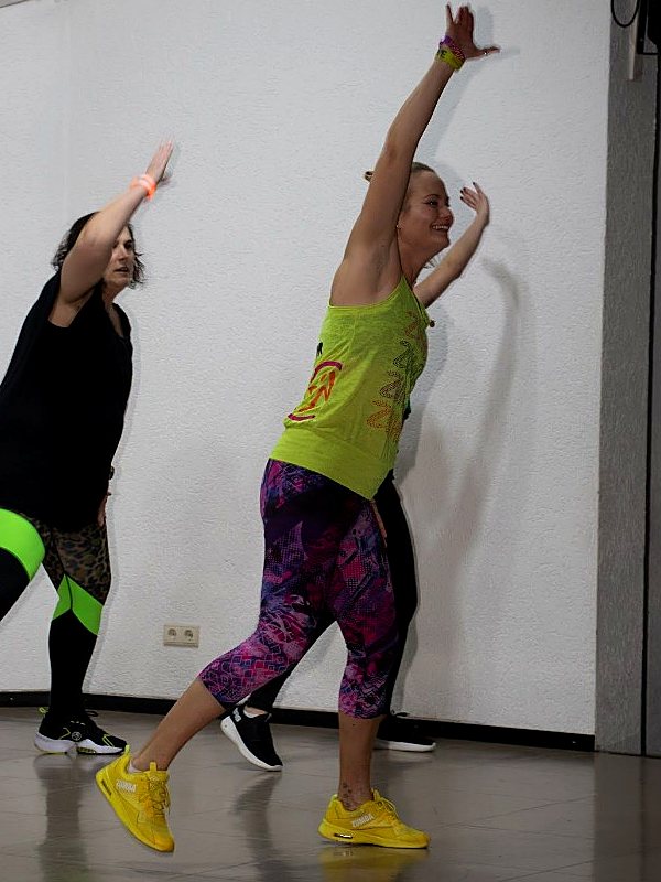 Zumba®-Moves im Kurs, Instructorin mit erhobenen Armen